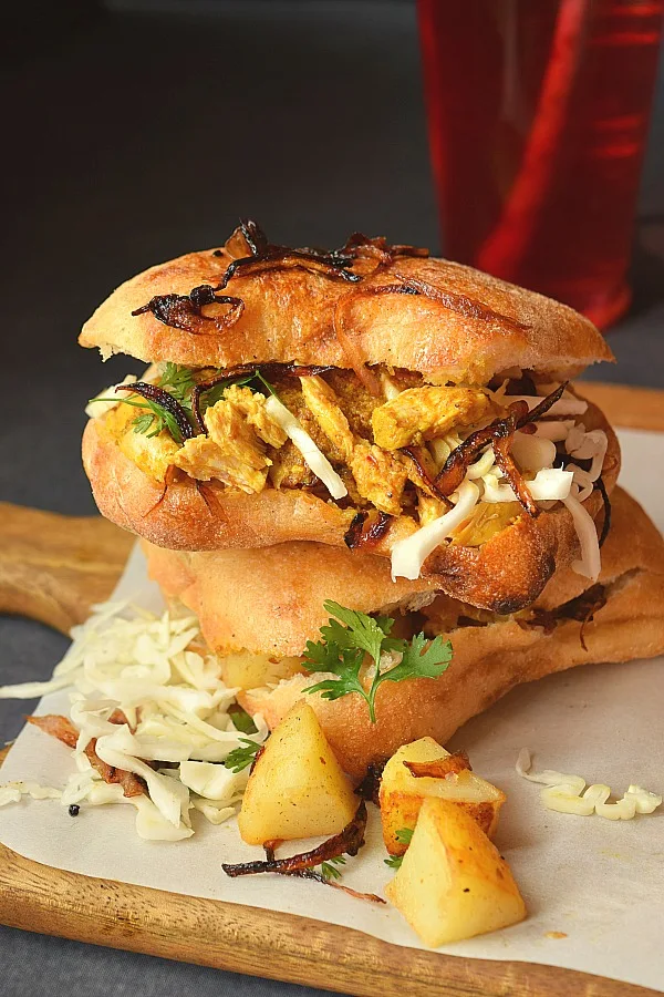 A wooden board with chicken sandwich,caramelized onions and butters potato chunks