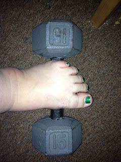 Photo of a steel 15lb dumbbell sitting on brown carpet with a pale foot resting on it