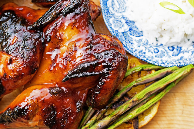 The grilled Cornish hen, on a cutting board with asparagus, and a plate of rice.  