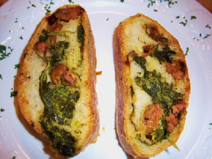 This is a homemade pizza dough stuffed with an Italian green called broccoli rabe with added cooked Italian sausage then added to that filling shredded whole milk mozzarella cheese. It is rolled up and baked into this golden crust then sliced like a sandwich with the filling in the middle.
