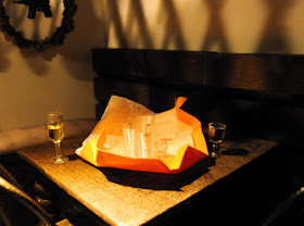 Modern one-twelfth scale miniature scene with two glasses of wine on a table and an unwrapped present between them.