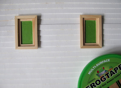 Undercoated wall of a dolls' house miniature kit, with windows covered with Frogtape.