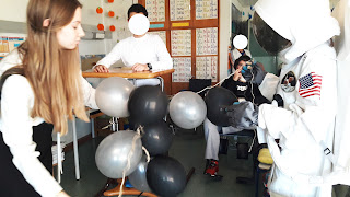 O astronauta e uma técnica assistente do Planetário levam um conjunto de balões cinzentos e pretos, símbolo da Cintura de Asteroides, até um aluno