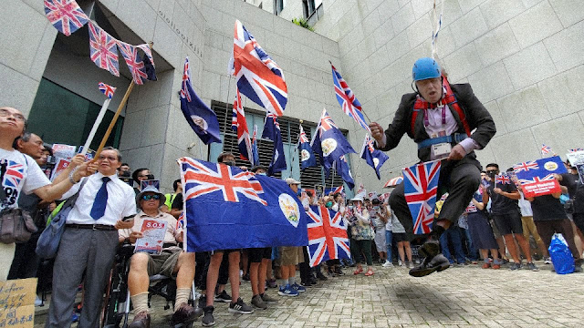An alternative version of events than that in the image above. Pictured close to the ground, British Prime Minister Boris Johnson is still suspended by a harness, but looks to be floundering badly. Hong Kongers surrounding him smile and continue to wave their Union Jack flags.