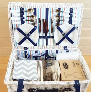 An open white picnic basket full of cutlery, plates and blue and white linens