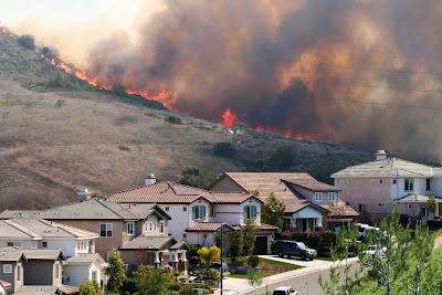 Image of wildfire burning on a hil with a residential neighboorhood at the foot of the hill.
