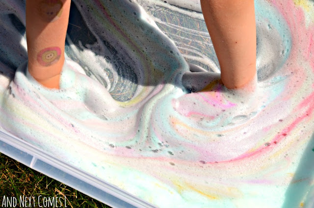 Close up of a toddler and preschooler playing with rainbow soap foam bubbles in a tie dye sensory bin
