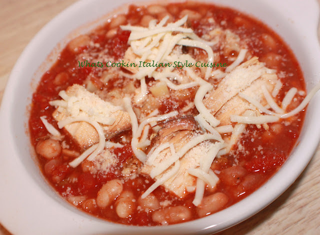 this is a bowl of pasta fagioli in a white dish topped with mozzarella and grated cheese. This pasta fagioli has chicken cubes in it and beans.