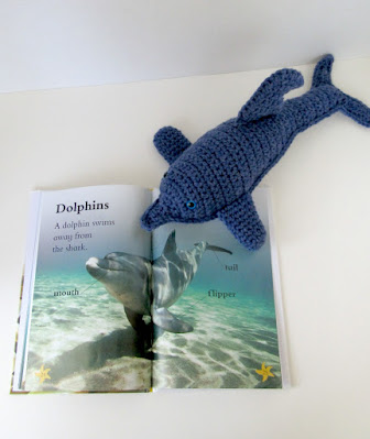 Plush toy dolphin reading the dolphin page in Fishy Tales
