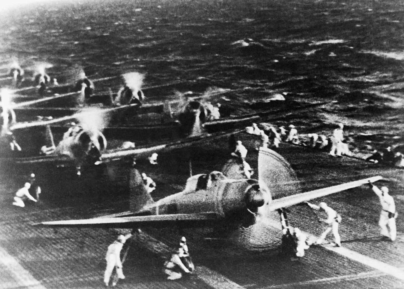 Dive bombers spin up on the deck of a carrier before taking off.