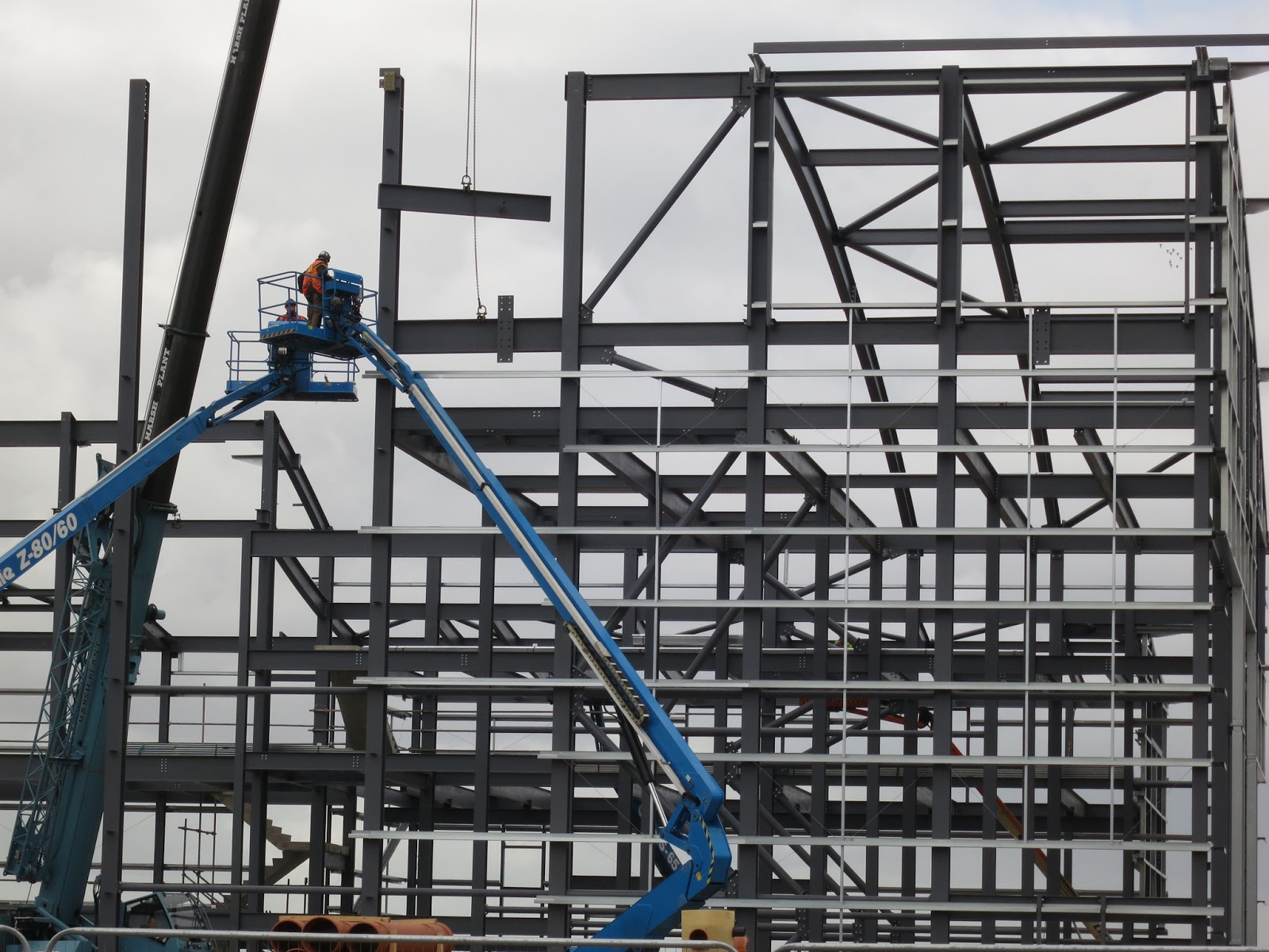 Two men, two blue hoists, large metal framework for building.