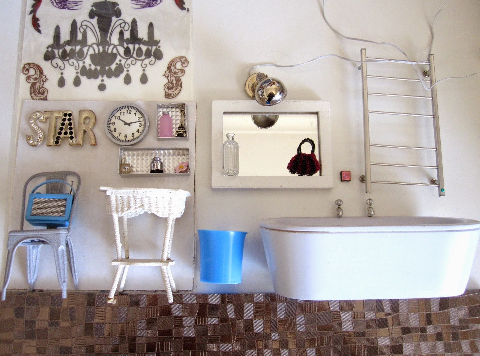 Selection of silver and white dolls house bathroom miniature furniture and accessories, with a full-sized silver-coloured placemat used as flooring and a range of silver, pink, white and blue miniature accessories.