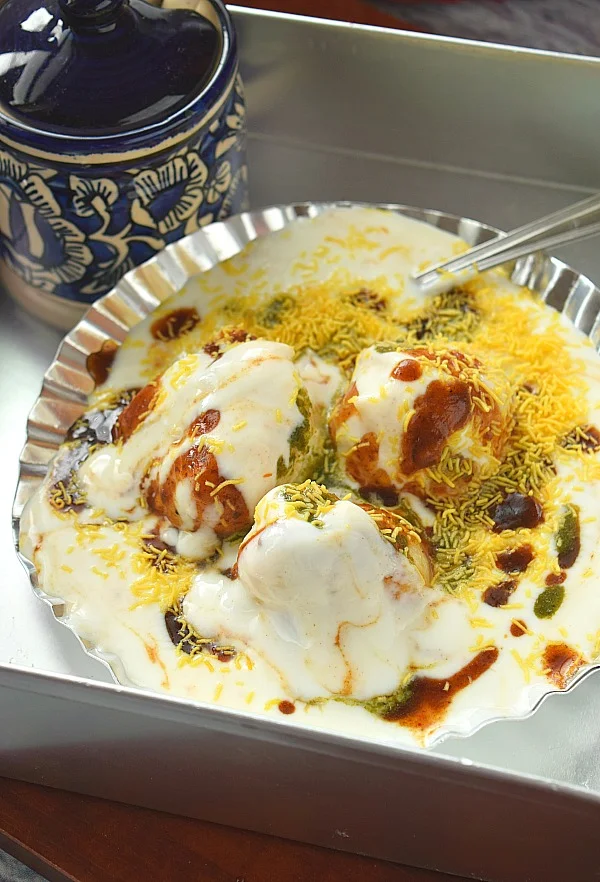 Close up of a silver plate served with soft Dahi Vada with sweet date chutney,Nylon Sev and Mint Chutney