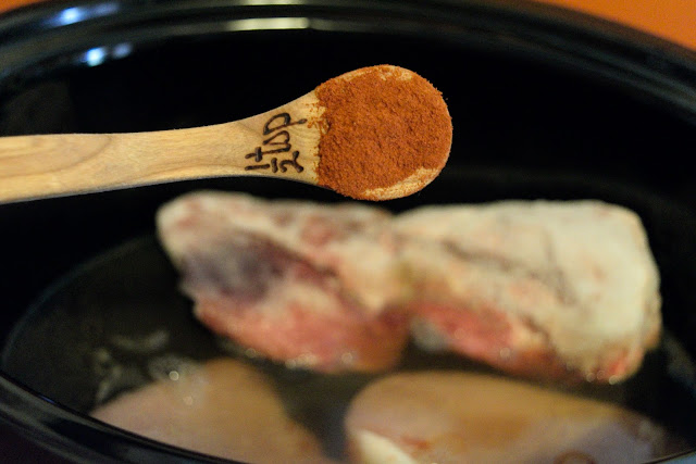 A measuring spoon filled with smoked paprika over the slow cooker.