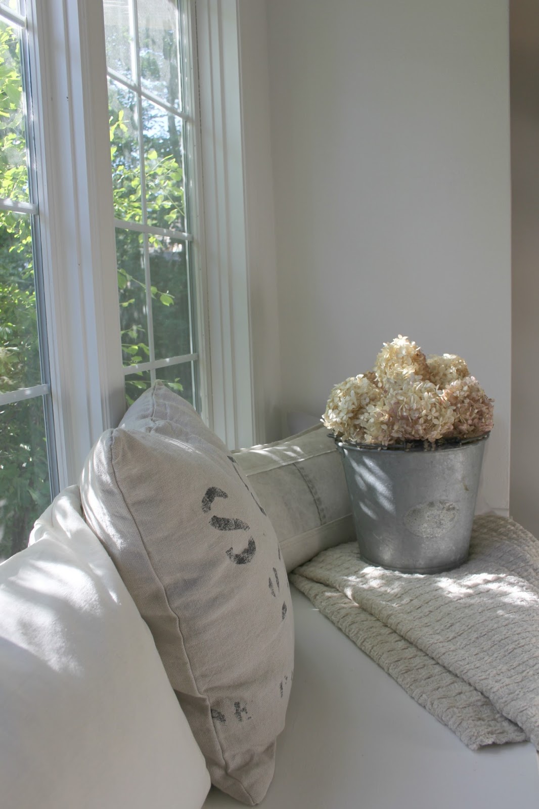 Hello Lovely's window seat in breakfast room of serene modern French kitchen. Belgian linen piillows and vintage galvanized pail holding dried hydrangea. Paint color is Bejamin Moore OC-151.