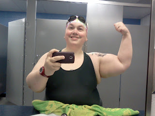 Post-swim self-photo in my swimsuit, cap, & goggles flexing my bicep