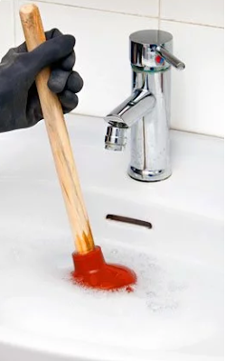 Stock photo of a red plunger used by a gloved hand in soapy water in a sink