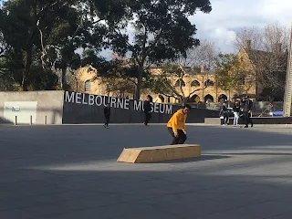Man in yellow hoodie skateboarding in front of the Melbourne Museum sign