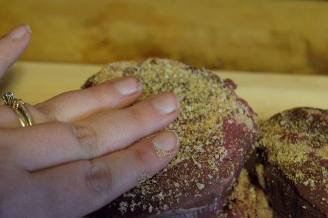 A steak with seasoning being rubbed into it. 