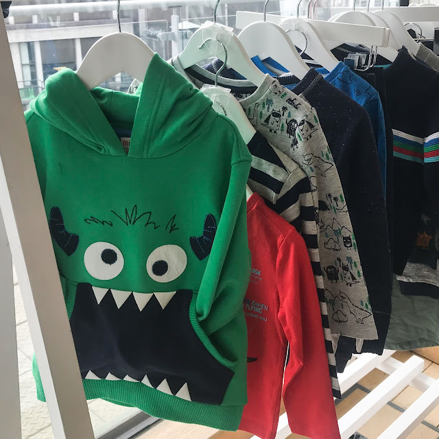 A rack of clothes with a green hoody at the front with a monster face