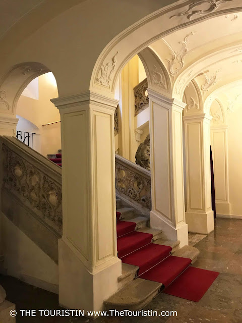 Staircase laid with red carpet in a vaulted entrance hall.