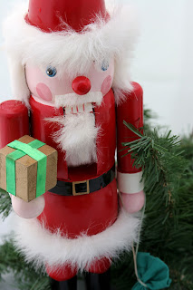 A Santa nutcracker nestled in pine branches against a white background