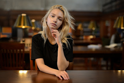 Chica pálida sentada en la biblioteca mirando a cámara