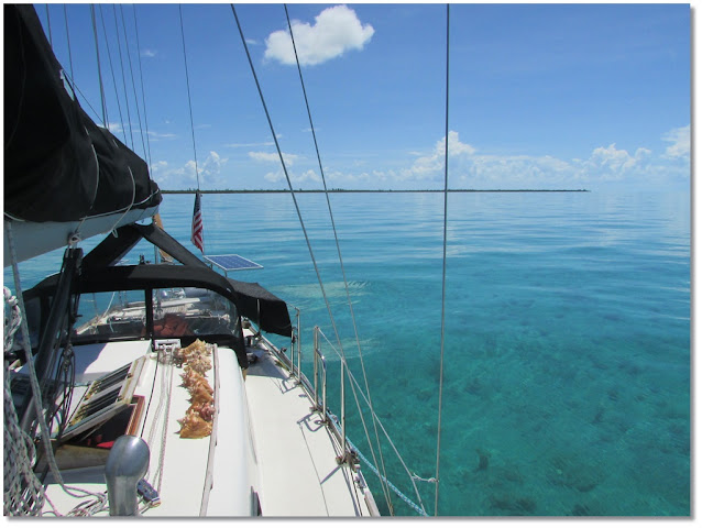 Sailboat floating on clam flat turquoise seas, facing the shore of Bimini.