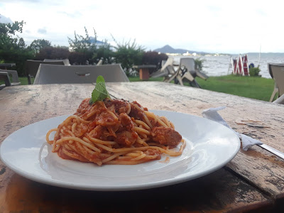 Spaghetti in red sauce and tuna on patio table by the sea