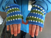 Lisa's hands (palms facing downwards) modelling fingerless mitts in horizontal stripes in Adelaide Oval colours. Solid stripes in mid blue and mid lime green are separated by horizontal rows of white dots.