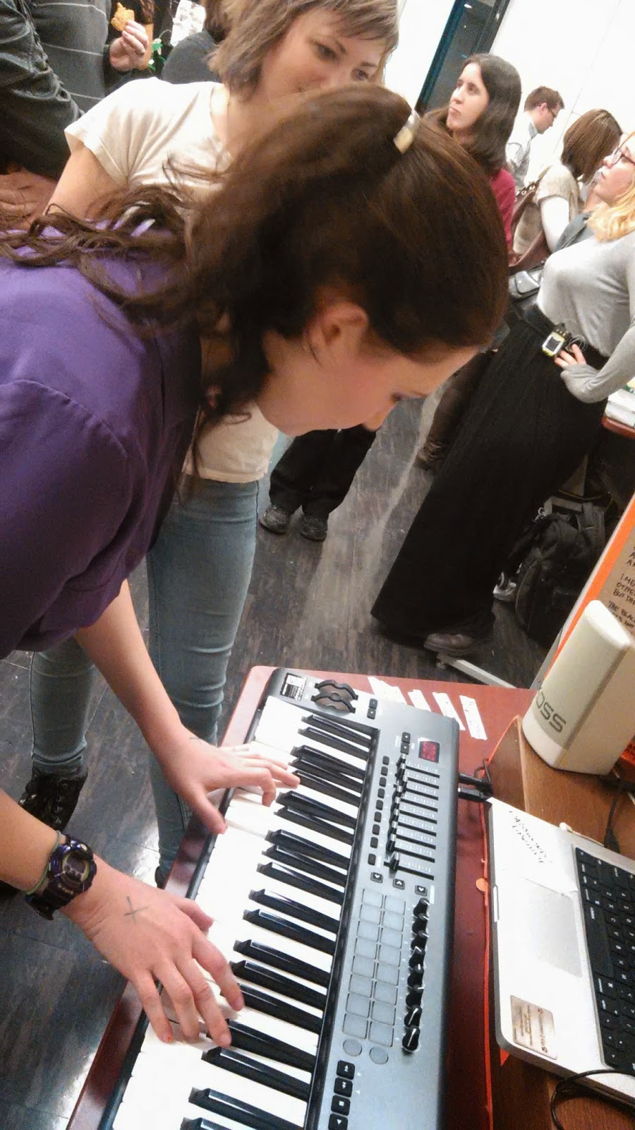 Photo of a woman playing a keyboard in a crowded room.