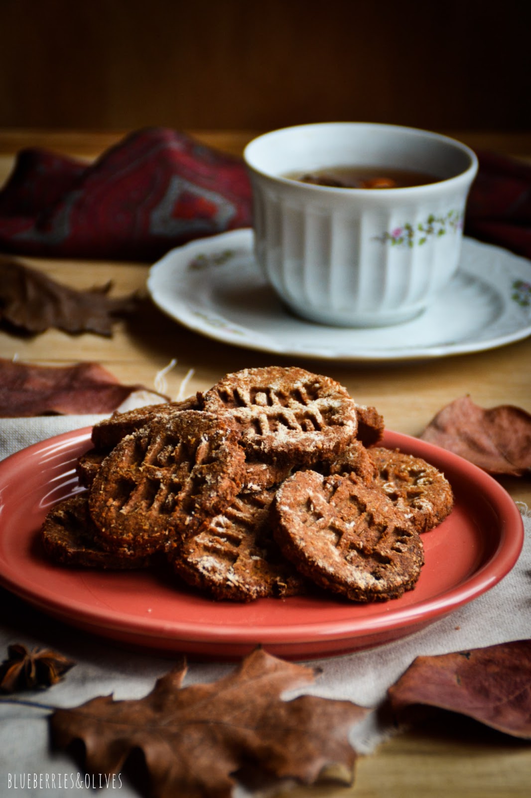Homemade cookies on red ceramic dish, dark background, old wood, piles books with red apple on top, porcelain mug with tea, star anise and orange peels