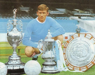 Tony Book e alcuni dei trofei vinti dal Manchester City tra il 1968 e il 1970: Campionato, FA Cup, Charity Shield.