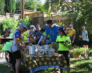 Cyclists loading their plates with the main course in a shady backyard.