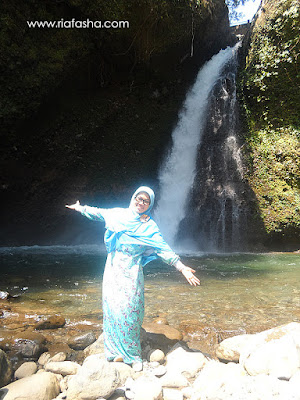 wanita berbaju biru berfoto di depan air terjun palak siring kemumu