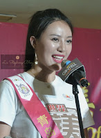 A female participant of the Miss Chinese World from Mongolia smilling happily in front of a microphone