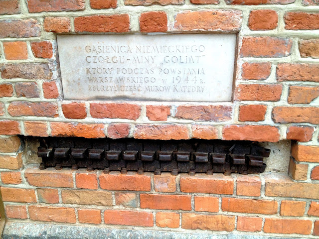 The embedded metal links below the plaque comprise a piece of the German tank 'Goliath' that was used during the Warsaw Uprising in '44. The plaque explains this and the fact that Goliath was responsible for the destruction of the Cathedral walls.