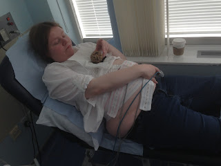 Helen on a hospital couch, holiding on one of the CTG transducers, eating a cupcake with a cup of coffee.