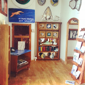 Miniature art gallery, with various items displayed for sale and a counter in one corner. On the wall is a sign saying 'the Royal Albatross art gallery'.