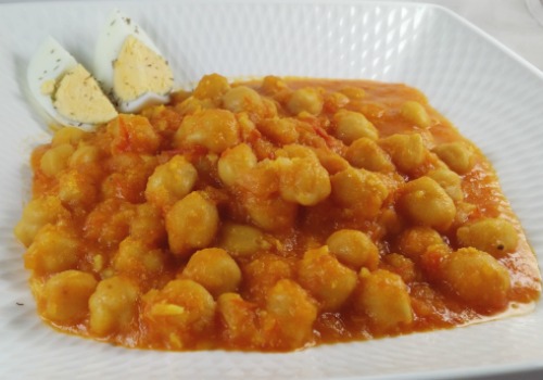 Unos garbanzos con salsa de tomate y adornados con huevo