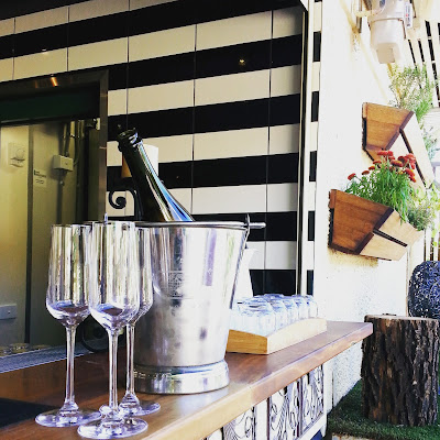 Bottle of sparkling wine in an ice bucket with three glasses on a bar.