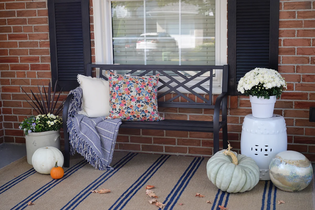 simple fall porch decor with striped rug and heirloom pumpkins