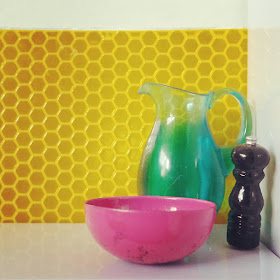 One-twelfth scale modern miniature still life with a water jug, bowl and pepper grinder against a wall of hexagonal tiles. 