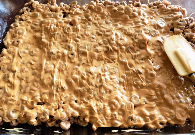 A picture of melted peanut butter being spread over top of cereal squares