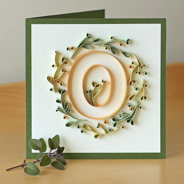 Quilled paper letter O surrounded by quilled leafy vine on greeting card