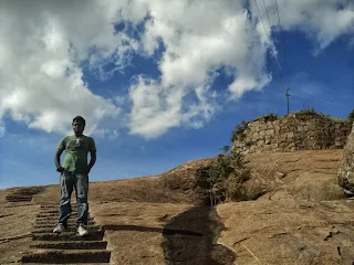 Hiker stands on step which leads to top of Hutridurga trek