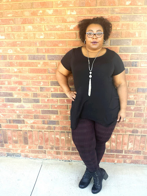 glam goth, long necklace, black tunic with sharkbite hem, maroon and black printed leggings, stacked combat booties, natural afro, hand on hip