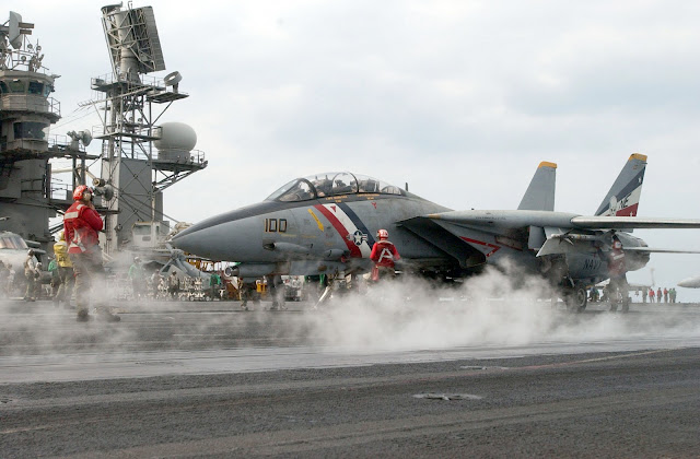 A flight deck crewmember guides an F-14D “Tomcat” assigned to the “Bounty Hunters” of Fighter Squadron Two (VF-2) onto one of four steam driven catapults on the ship’s flight deck.