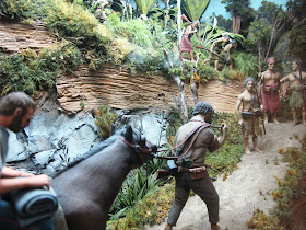 Diorama of a 19th-century man on the back of a horse in the bush,being lead up a track by a Maori.