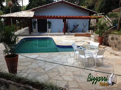 Construção de piscina de concreto revestida de azulejo em residência em condomínio em Atibaia-SP com o pergolado de madeira, o muro de pedra e o piso da piscina com pedra São Tomé tipo caco.